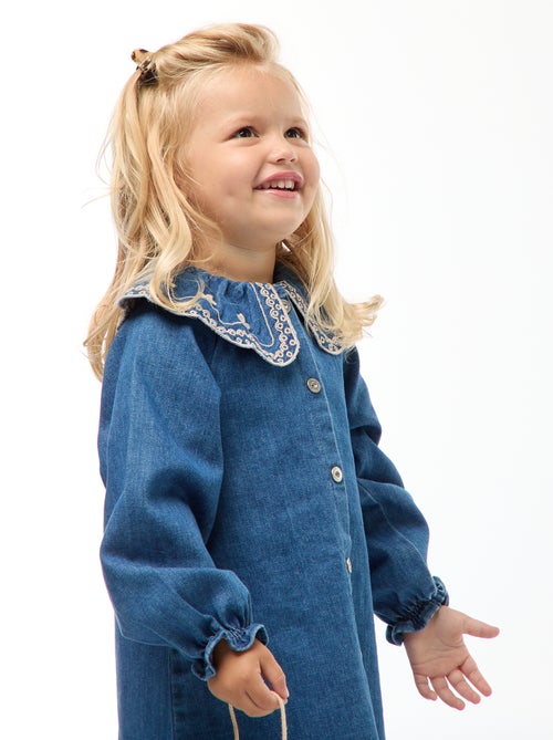 Robe-chemise enfant en denim bleu durable, avec boutons blancs et grand col rond brodé de motifs floraux, fabriquée en coton bio et matières recyclées.