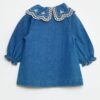 Robe-chemise enfant en denim bleu durable, avec boutons blancs et grand col rond brodé de motifs floraux, fabriquée en coton bio et matières recyclées.