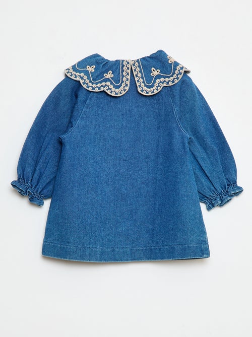 Robe-chemise enfant en denim bleu durable, avec boutons blancs et grand col rond brodé de motifs floraux, fabriquée en coton bio et matières recyclées.